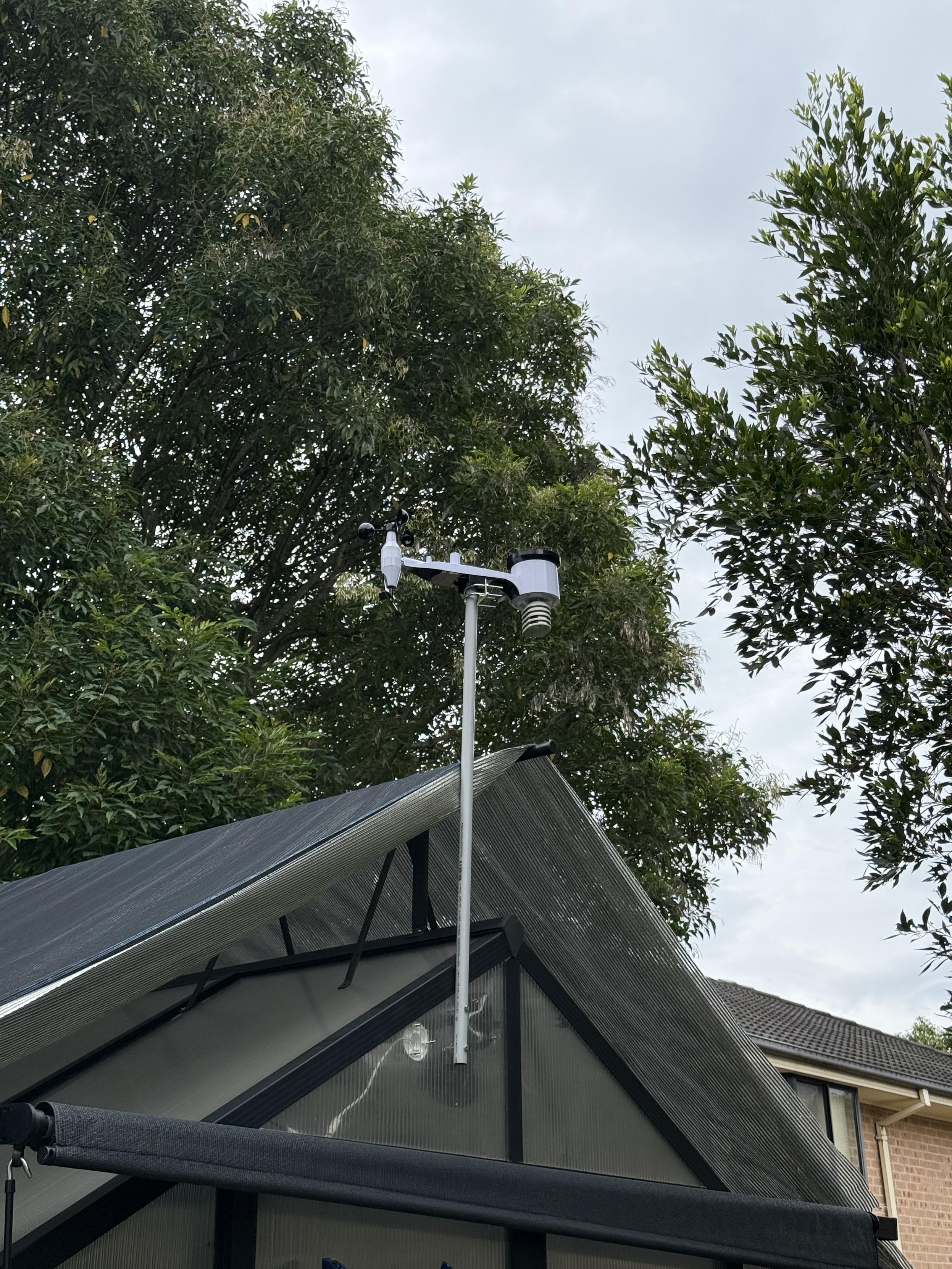 Ecowitt WS69 weather station sensor array mounted on conduit above a greenhouse